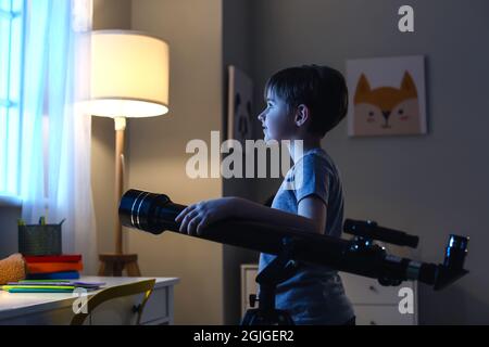 Kleiner Junge, der am Abend durch das Teleskop Sterne anschaut Stockfoto