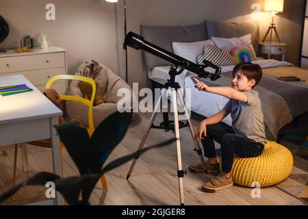 Kleiner Junge, der am Abend durch das Teleskop Sterne anschaut Stockfoto