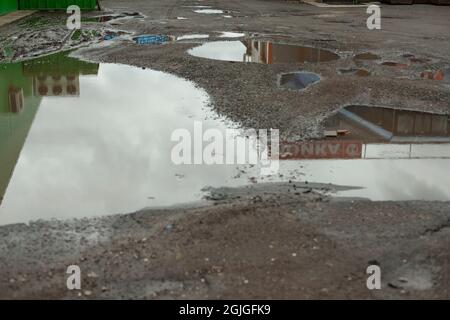 Schmutzige Pfütze auf der Straße. Gruben auf dem Parkplatz. Schlechter Asphalt mit Schlaglöchern. Typisch russische Straße in der Stadt. Stockfoto