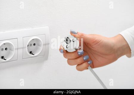 Eine Frau steckt den Stecker in die Steckdose im Zimmer Stockfoto