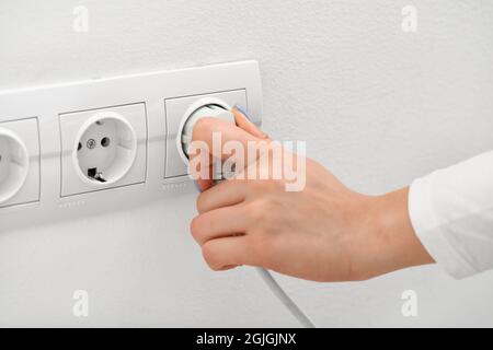 Eine Frau steckt den Stecker in die Steckdose im Zimmer Stockfoto
