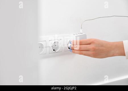 Eine Frau steckt den Stecker in die Steckdose im Zimmer Stockfoto