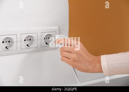 Eine Frau steckt den Stecker in die Steckdose im Zimmer Stockfoto
