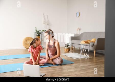 Kleines Mädchen mit ihrer Mutter, die zu Hause Yoga praktiziert Stockfoto