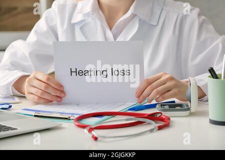 Ärztin, die in der Klinik Papier mit Text FÜR HÖRVERLUST hält Stockfoto