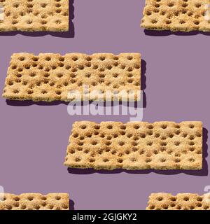 Foto in Form eines nahtlosen Musters. Orangefarbene Knäckebrot für gesunde Lebensmittel mit Schatten auf einem farbigen lila Hintergrund. Stockfoto