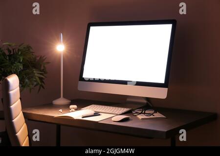 Moderner Arbeitsplatz mit Computer und glühender Lampe im dunklen Raum Stockfoto