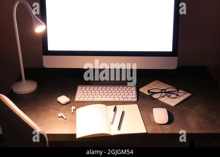 Moderner Arbeitsplatz mit Computer und glühender Lampe im dunklen Raum Stockfoto