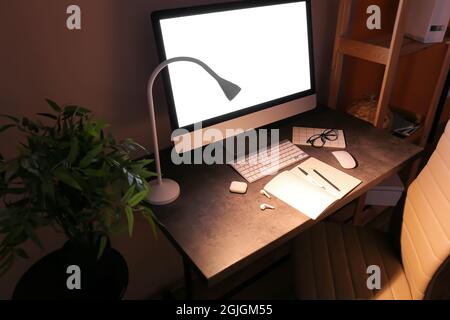 Moderner Arbeitsplatz mit Computer und glühender Lampe im dunklen Raum Stockfoto