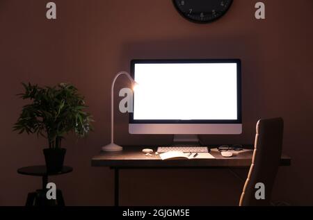 Moderner Arbeitsplatz mit Computer und glühender Lampe im dunklen Raum Stockfoto