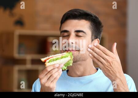 Junger Mann, der zu Hause leckeres Sandwich isst Stockfoto