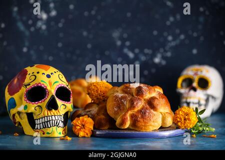 Brot der Toten und bemalter Schädel auf farbigem Hintergrund. Feier des mexikanischen Tages der Toten (El Dia de Muertos) Stockfoto