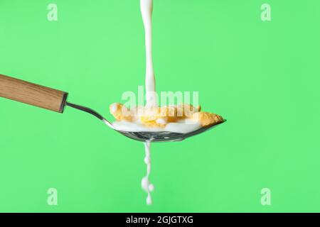 Gießen von Milch in Löffel mit Cornflakes auf farbigem Hintergrund, Nahaufnahme Stockfoto