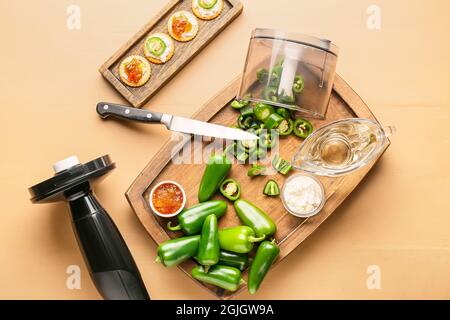 Mixer und Zutaten für köstliche Jalapeno-Pfeffermarmelade auf farbigem Holztisch Stockfoto