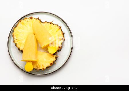 Teller mit leckeren Ananaspopsicles auf weißem Hintergrund Stockfoto