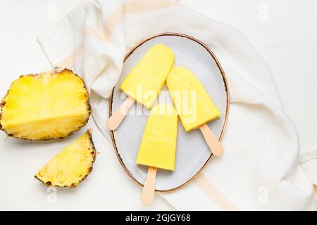 Teller mit leckeren Ananaspopsicles auf hellem Hintergrund Stockfoto