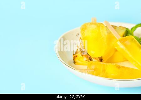 Teller mit leckeren Ananaspopsicles auf farbigem Hintergrund Stockfoto