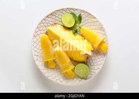 Teller mit leckeren Ananaspopsicles auf weißem Hintergrund Stockfoto