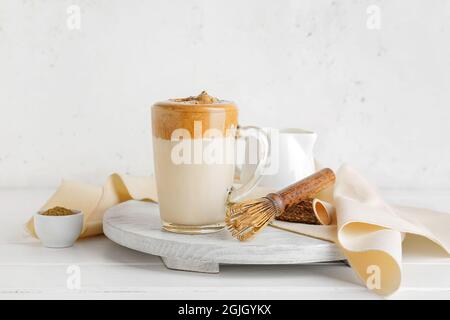 Glastasse mit leckeren dalgona hojicha Latte und Chasen auf hellem Hintergrund Stockfoto