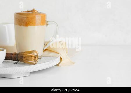 Glastasse mit leckeren dalgona hojicha Latte und Chasen auf hellem Hintergrund Stockfoto