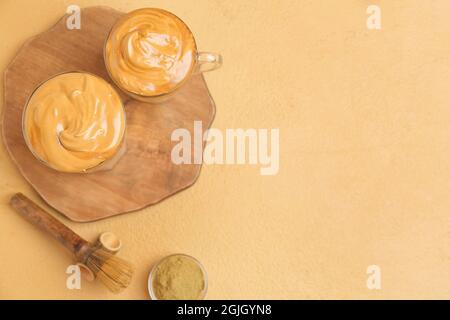 Glas und Tasse leckeren dalgona hojicha Latte mit Chasen auf farbigem Hintergrund Stockfoto