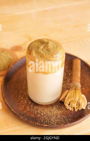 Ein Glas leckeren dalgona hojicha Latte und Chasen auf Holzboden Stockfoto