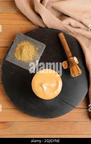 Ein Glas schmackhaften dalgona hojicha Latte, Chasen und Pulver auf hölzernen Hintergrund Stockfoto