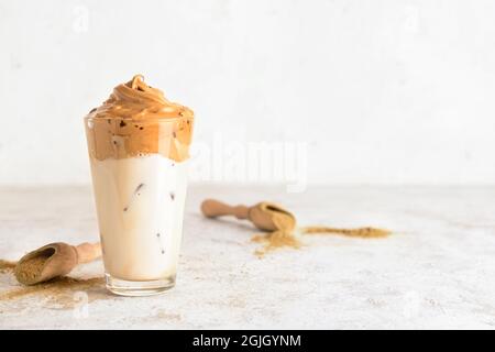 Ein Glas leckeren dalgona hojicha Latte und Pulver auf hellem Hintergrund Stockfoto