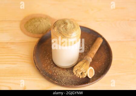 Ein Glas leckeren dalgona hojicha Latte und Chasen auf Holzboden Stockfoto