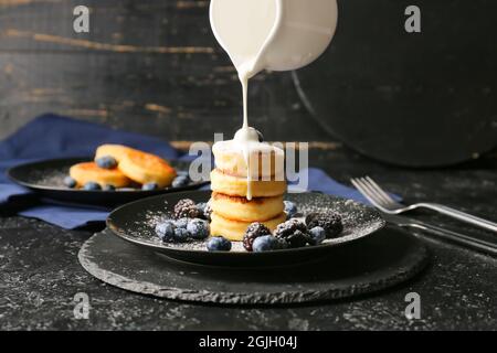 Gießen Sie Kondensmilch auf den Teller mit Quark-Pfannkuchen auf dem Tisch Stockfoto