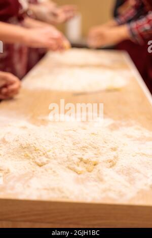 Die Hände mehrerer Personen kneten den Teig auf dem Tisch. Ein rohes Ei mit Mehl vermischen. Nahaufnahme. Stockfoto