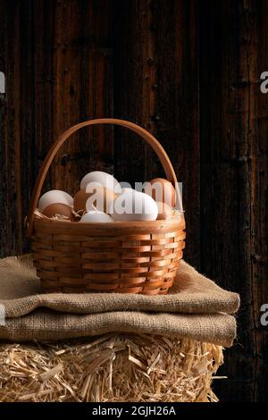 Eine kleine Holzkiste aus frisch gesammeltem Ei, die auf einer Sackleine sitzt, und ein Heuballen in einer Scheune. Das Bild zeigt die Frische, die mit dem Landleben verbunden ist. Stockfoto