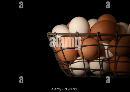 Ein kleiner Korb mit frischen, braunen und weißen Eiern während des Sonnenaufgangs, der bei einer traditionellen Bauerngemeinschaft gesammelt wurde. Stockfoto