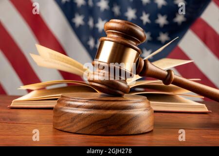 Auf dem Schreibtisch eines Richters mit einem Buch und amerikanischer Flagge steht ein Holzblock und ein Gavel. Stockfoto