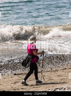 Frau, die mit Wanderstöcken am Ufer entlang läuft. Konzept des Foto aktiven Lebensstils im Alter, Street View, Reisefoto, selektiver Fokus, Kopie sp Stockfoto