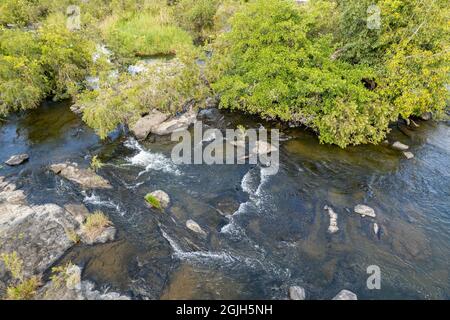 Wasser fließt über Felsen auf flachem Flussbett zwischen Bäumen, Drohnenlandschaft Luftbild Stockfoto