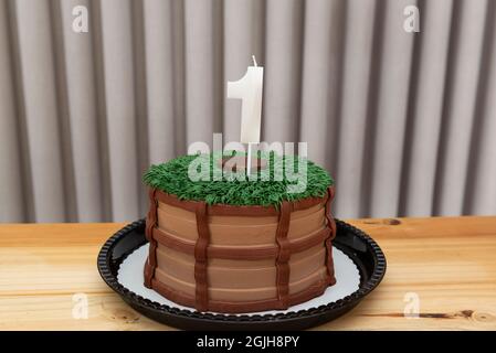 Dekorierter Schokoladenkuchen. Eine einjährige weiße Kerze auf Kuchen, dekoriert im Landhausstil auf einem hellen Holztisch. Stockfoto