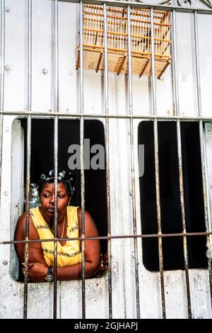 Kubanische Frau mit Vogel im Vogelkäfig, die durch die Fensterstangen ihres Hauses, Sancti Spiritus, Kuba, schaute Stockfoto