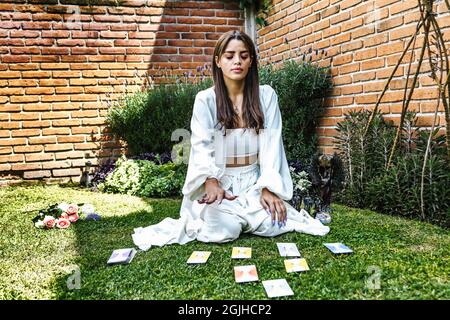 Mexikanisches Mädchen mit Tarot-Karten und andere Objekte als alternative Therapie im Garten in Lateinamerika Stockfoto