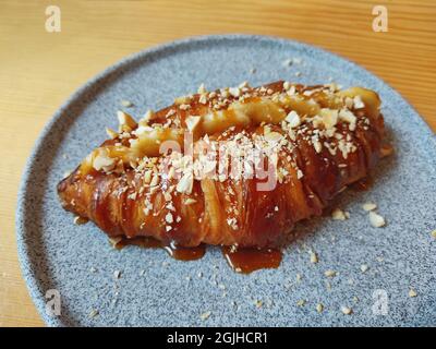 Frisch gebackene süße Croissants mit Karamell und Banane auf einem grauen Teller auf dem Tisch Stockfoto