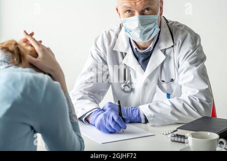 Covid-19, Prävention von Viren, medizinisches Personal und Impfkonzept. Seriös zuversichtlich männlichen Arzt in weißem Mantel und medizinische Maske, trägt eine Brille, Stockfoto