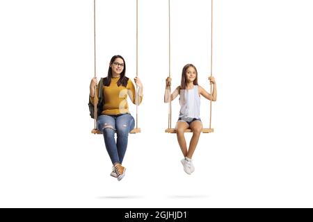 Junge Studentin und ein Mädchen sitzen auf Schaukeln und betrachten die Kamera isoliert auf weißem Hintergrund Stockfoto