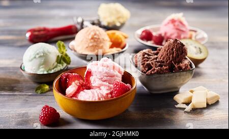 Hoher Winkel von köstlichen bunten Eis Schaufel mit verschiedenen Geschmacksrichtungen auf Holztisch in Schüsseln platziert Stockfoto