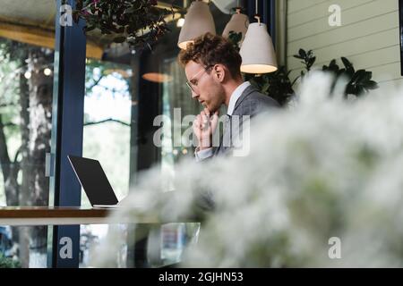 Nachdenklicher Geschäftsmann im Anzug mit Laptop mit leerem Bildschirm im Café Stockfoto