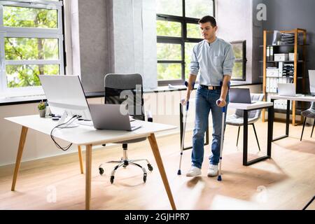 Arbeiter Mit Krücken Am Arbeitsplatz Oder Im Büro. Leistungen Für Die Rehabilitation Bei Handicap Stockfoto