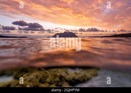 Split Shot, über unter der Wasseroberfläche. Unschärfe-Wellen im Vordergrund mit Tavolara Island an der Oberfläche während eines dramatischen Sonnenaufgangs. Stockfoto