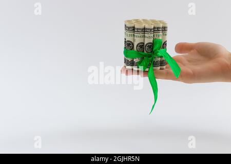 Weibliche Hand hält rollte 100-Dollar-Banknoten mit grünem Geschenkband gebunden. Stockfoto