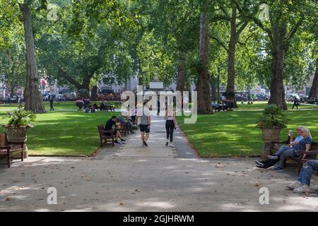 Menschen unterwegs und entspannen an einem sonnigen Sommertag in den Berkeley Square Gardens, Mayfair, London, England, Großbritannien Stockfoto