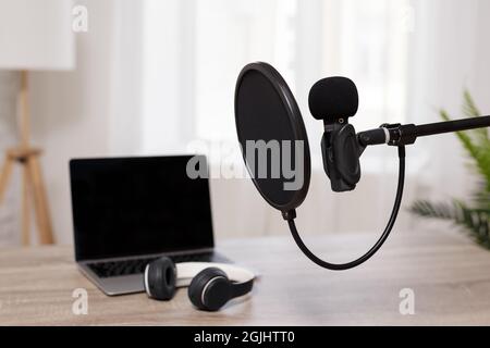 Podcast, Sprachaufzeichnung und Blogging-Konzept - Nahaufnahme des Mikrofons mit POP-Filter und Laptop mit Kopierplatz auf dem Bildschirm im hellen Home Office Stockfoto