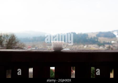 Eine weiße Tasse steht auf dem Balkongeländer mit einem Panorama auf die Stadt und niedrige Berglandschaft im Hintergrund Stockfoto
